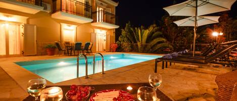 A poolside dining area with a table set for two, a pool, and a building with balconies.