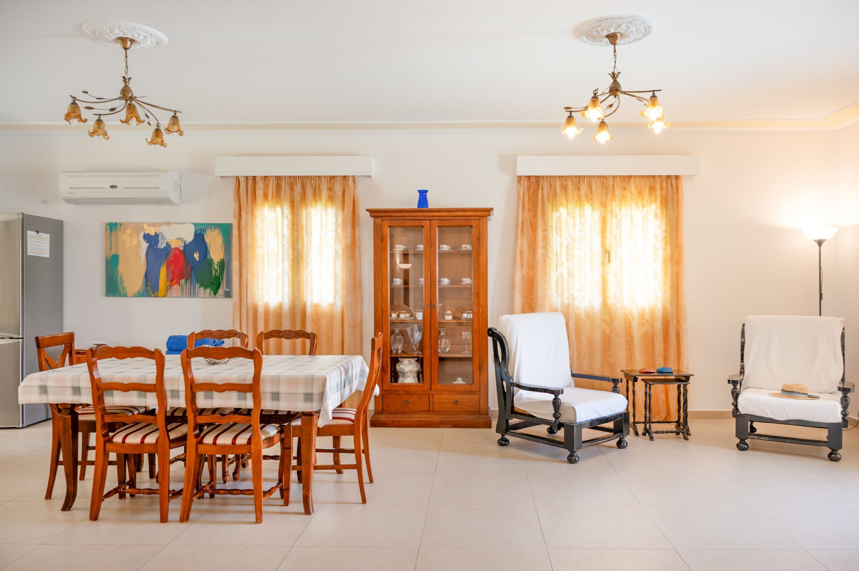 Un comedor con una mesa, sillas, un aparador con puertas de vidrio y una silla de ruedas.