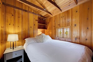 A wooden room with a bed, a nightstand, a lamp, and a window with stained glass.