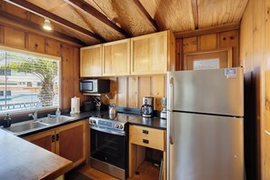 A compact kitchen with wooden cabinets, a stainless steel refrigerator, a stove, and a microwave.