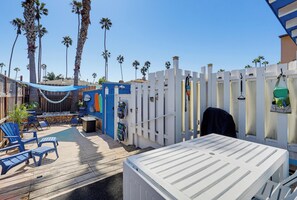 A deck with outdoor seating and a pool, surrounded by palm trees and a white fence.