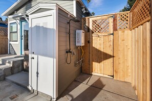 Un espace douche extérieur compact, doté d’une clôture en bois, d’une porte et d’un chauffe-eau.