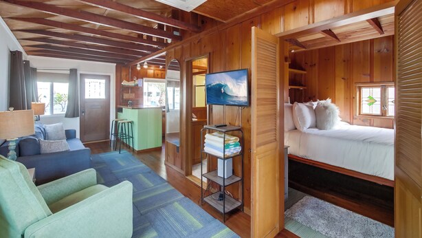 Un interior cálido de cabaña con cama, sofá, televisor y una zona de cocina.