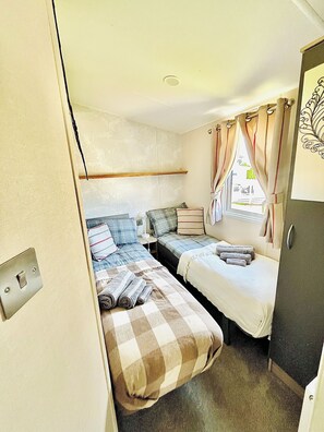 Un dormitorio pequeño con dos camas, una ventana con cortinas, un estante en la pared y una puerta con panel decorativo.