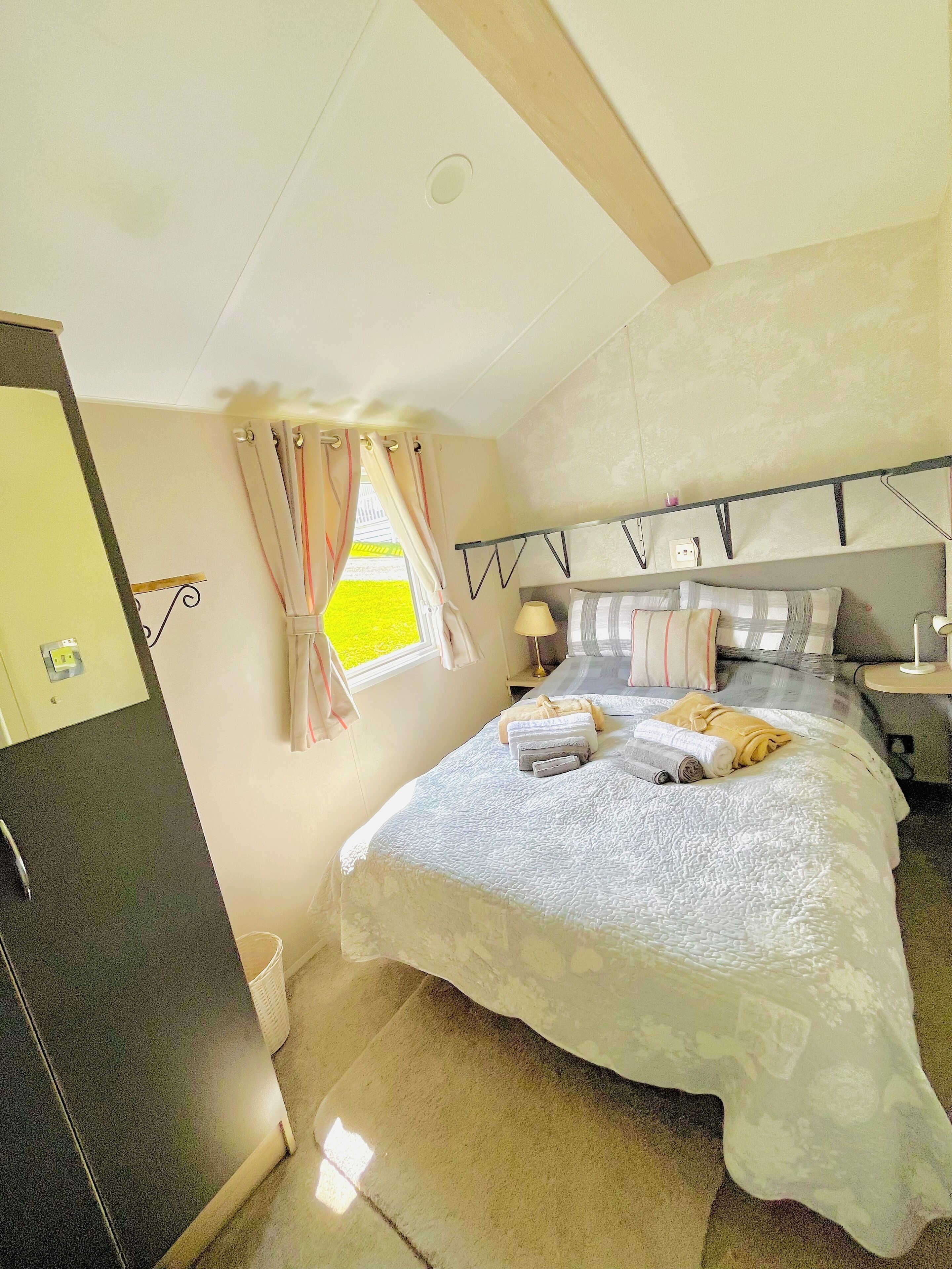 A bedroom with a bed, bedside tables, a window with curtains, a ceiling light, and a door.