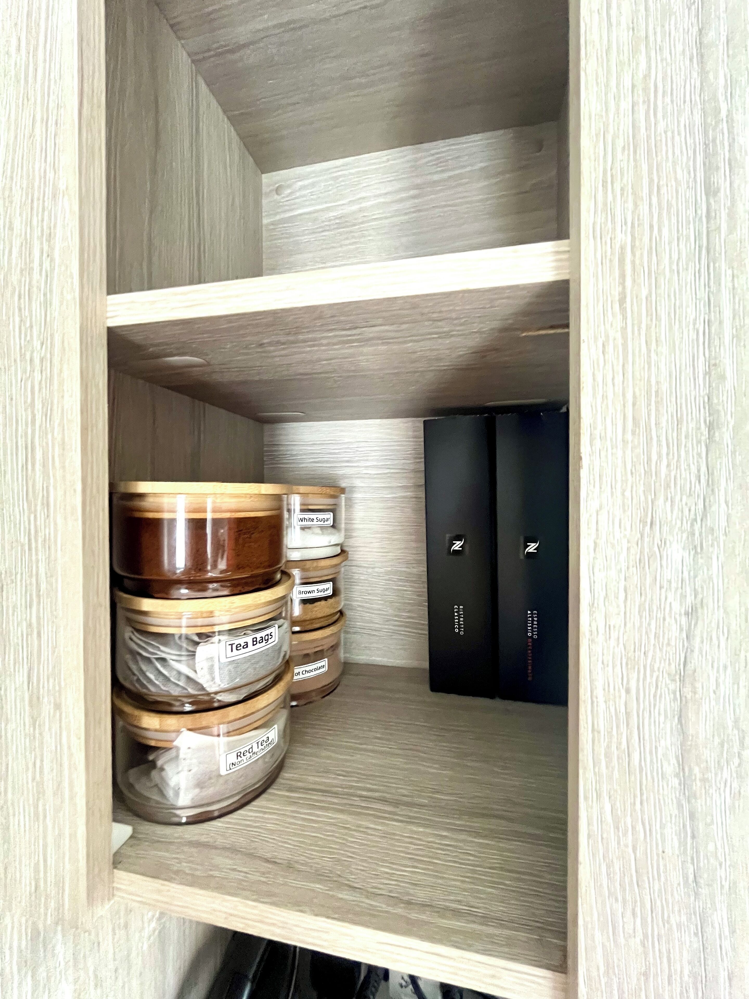 A wooden shelf with jars labeled 'White Sugar', 'Brown Sugar', 'Tea Bags', and 'Hot Chocolate'.