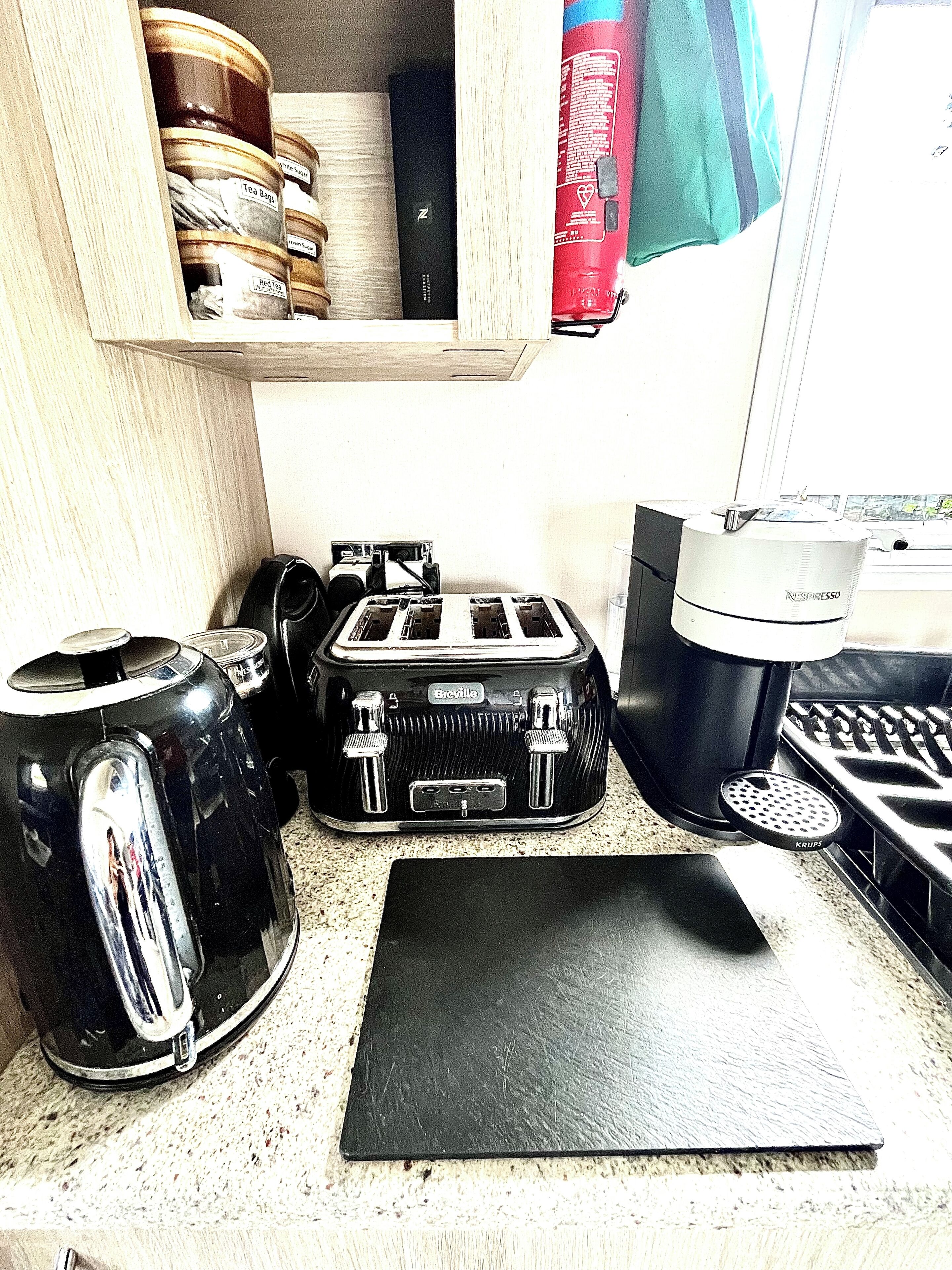 Une petite cuisine équipée d’une machine à café, d’un grille-pain et d’une planche à découper noire posée sur le plan de travail.