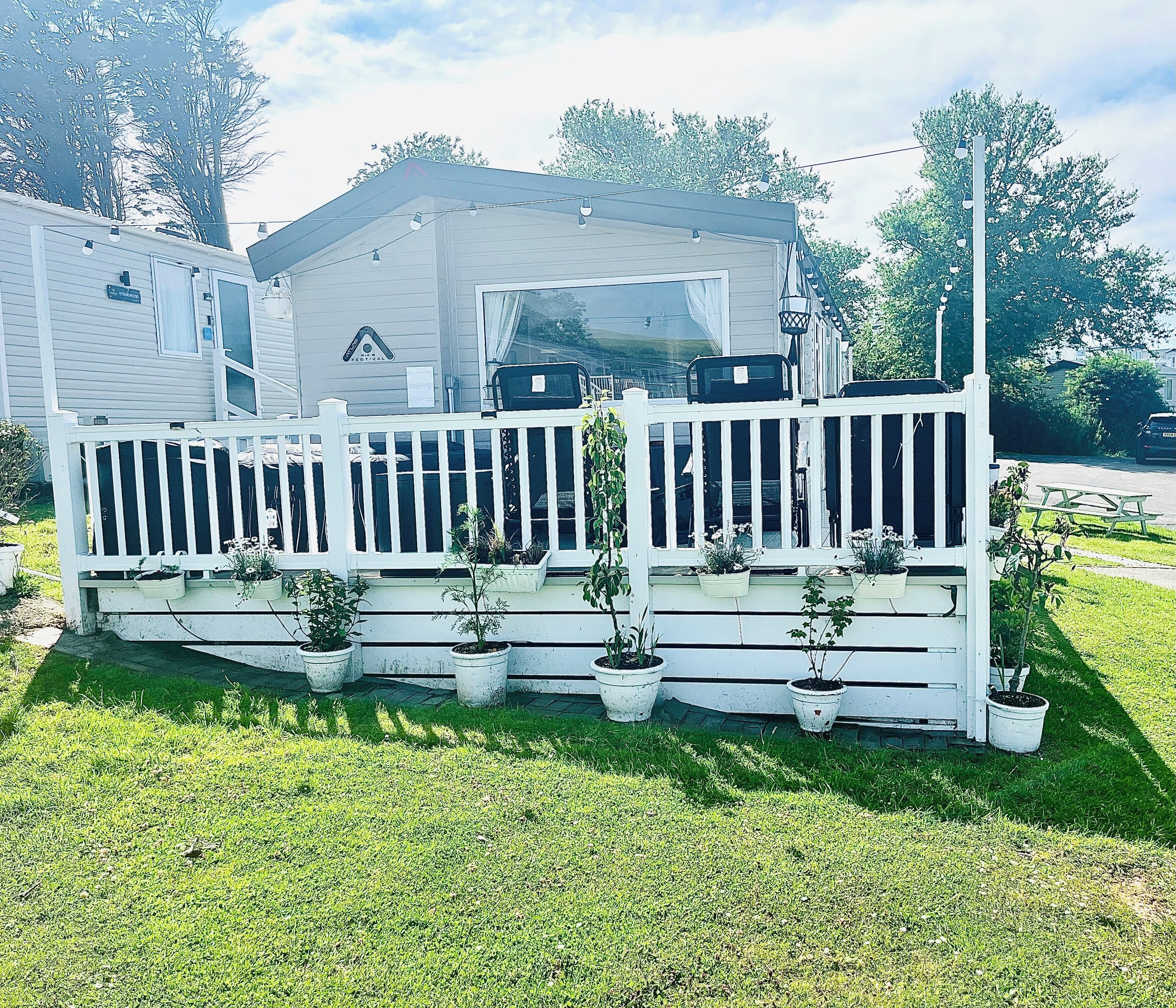 A mobile home with a white porch, potted plants, and a picnic table.