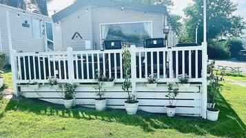 A mobile home with a white porch, potted plants, and a picnic table.