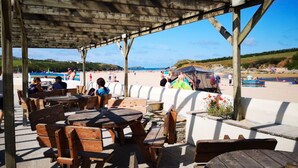 Un espacio de estar al aire libre con mesas y bancos de madera, con vista a una playa.