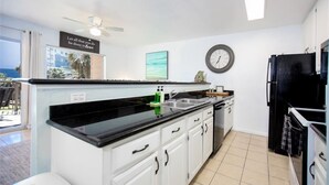 Une cuisine avec des meubles blancs, un plan de travail noir, un réfrigérateur noir et une horloge au mur.