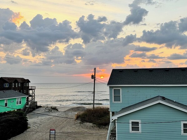 A coastal scene with a sunset, a beach, and two houses.