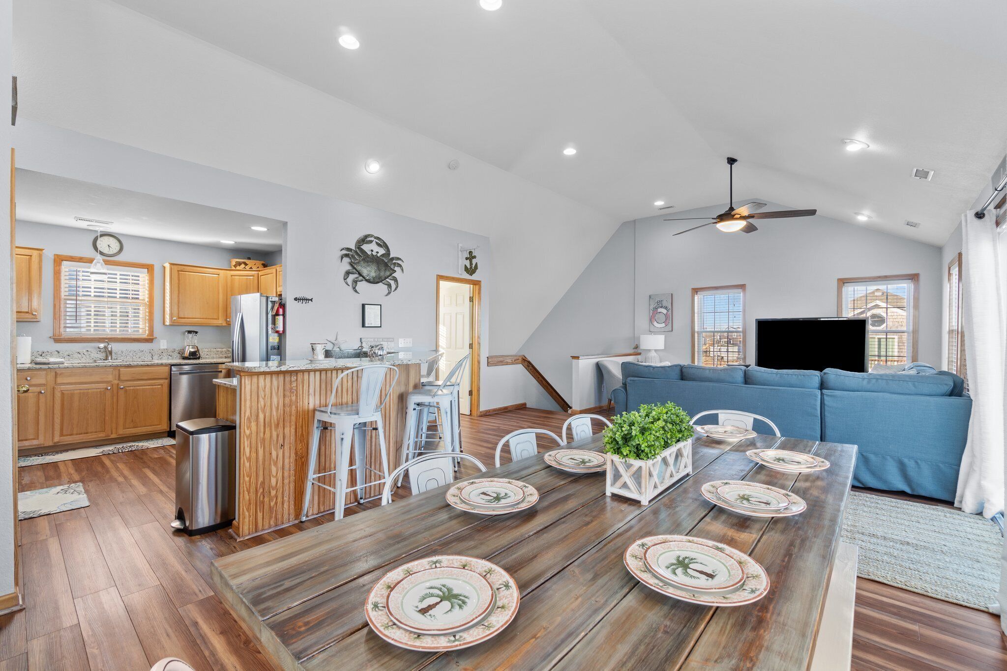 A spacious kitchen with wooden cabinets, a dining area with a wooden table set for four, and a blue sofa in the living area.