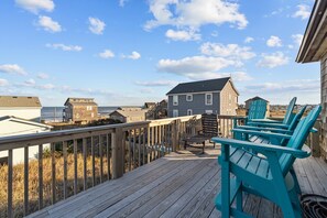 A wooden deck with chairs overlooking a beach and houses.