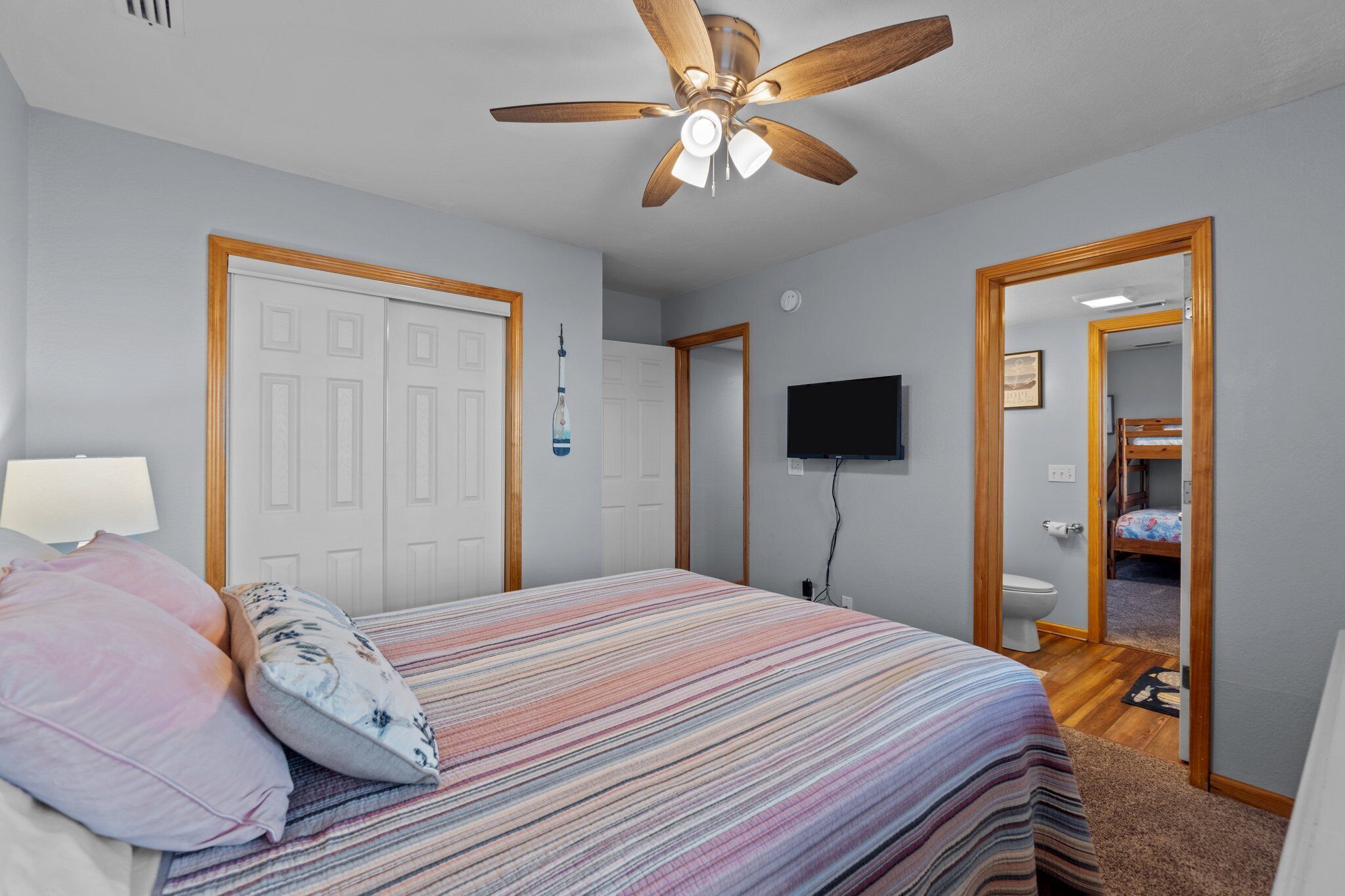 Une chambre à coucher comprenant un lit, un ventilateur de plafond, une télévision et une porte donnant accès à une salle de bain.