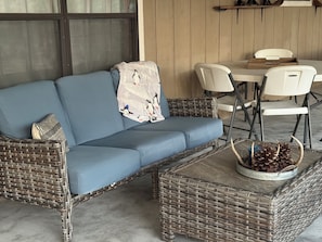 A wicker sofa with a blue cushion, a small round table with pine cones, and white chairs.