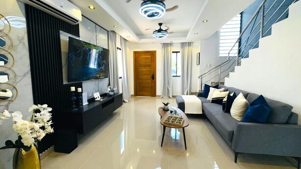 A modern living room with a flat-screen TV, a ceiling fan, and a staircase. - Tranquil villa with AC and pool in Punta Cana (Punta Cana)