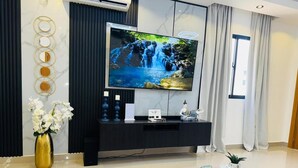 A modern living room with a large flat-screen TV, a black entertainment unit, a round coffee table, and a vase of white flowers. - Tranquil villa with AC and pool in Punta Cana (Punta Cana)