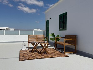 Eine Dachterrasse mit zwei Holzstühlen, einem kleinen Tisch, einem Blumentopf und einem Laternen.