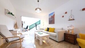 A modern living room with a sofa, a coffee table, a chair, and a small table with a lamp. There is a staircase leading to another room. - Casa Casa NoPasaNada, habitación Triple Los Lobos (Tinajo)