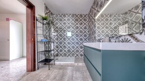 Un baño con salpicadero de azulejos estampados, repisa de vidrio con toallas y un mueble azul.