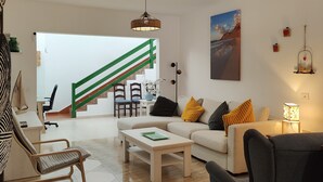 Una sala de estar moderna con sofá, mesa de centro y sillas. Una escalera con barandillas verdes conduce a otra habitación.