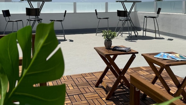 A rooftop terrace with tables and chairs, potted plants, and a view of the city skyline.