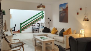 A modern living room with a sofa, coffee table, and chairs. A staircase with green railings leads to another room.