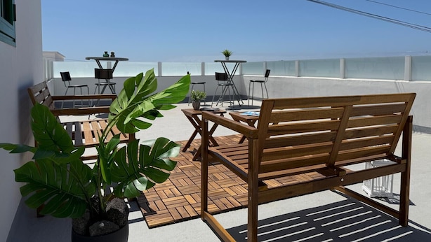 A rooftop terrace with a wooden bench, a table with chairs, and potted plants.