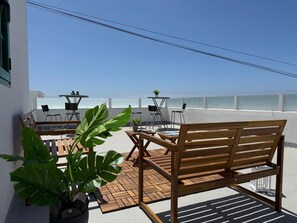 Una terraza en la azotea con un banco de madera, una mesa con sillas y plantas en macetas.