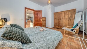 Un dormitorio con cama, almohadas, un armario de madera, una silla y un espejo.
