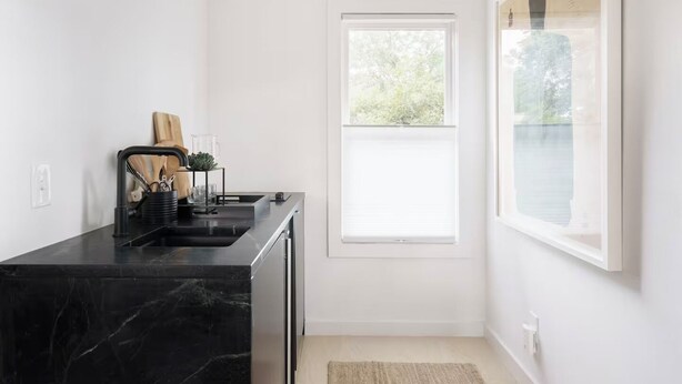 A modern kitchen with a black marble countertop, a sink, and a window with a view of greenery. - High-style Home near Bishop Arts and Downtown Dallas (Dallas)