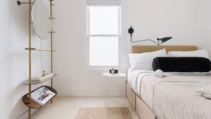 Een slaapkamer met een bed, nachtkastje, lamp en een raam.