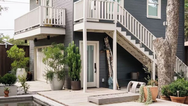 Een huis met twee verdiepingen, een balkon en een wenteltrap naar de bovenverdieping, met een zwembad op de voorgrond.
