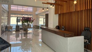 Un espace d'accueil moderne avec un comptoir de réception en marbre poli, un coin salon avec des fauteuils et un mur en bois à lattes.