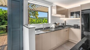 A modern kitchen with a large window, built-in appliances, and a view of greenery. - Lounge Appart A refined, discreet, carefully designed space (VAUCLIN)