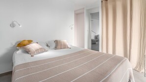 A bedroom with a bed, two pillows, a bedside lamp, and a window with curtains. - Lounge Appart A refined, discreet, carefully designed space (VAUCLIN)
