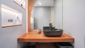 A modern bathroom with a wooden vanity, a large mirror, and a black vessel sink. - Lounge Appart A refined, discreet, carefully designed space (VAUCLIN)