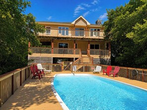 A two-story building with a swimming pool, deck chairs, and a wooden fence.