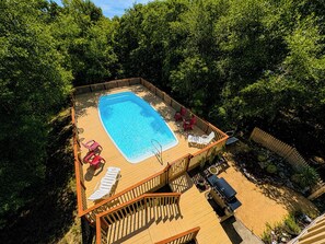 A rooftop pool with a wooden deck, surrounded by trees.