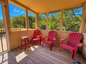 A covered porch with wooden flooring and red Adirondack chairs.