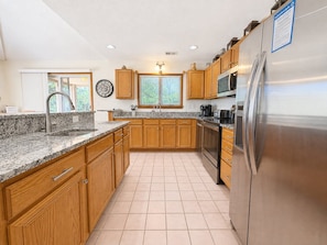 A kitchen with wooden cabinets, a stainless steel refrigerator, and a granite countertop.