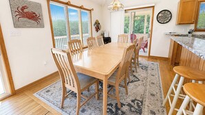 A dining area with a wooden table and chairs, a rug, and a view through a window.