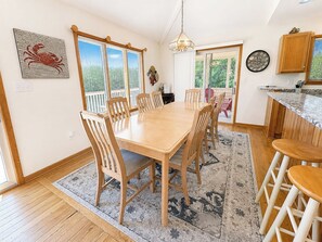 A dining area with a wooden table and chairs, a rug, and a view through a window.