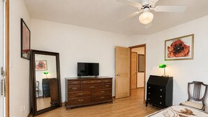 A bedroom with a bed, dresser, television, and a ceiling fan.