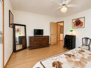 A bedroom with a bed, dresser, television, and a ceiling fan.