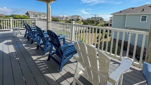 Una terraza de madera con sillas Adirondack azules y blancas, una mesita y una barandilla blanca.
