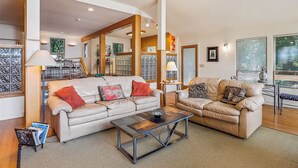 A spacious living room with two beige sofas, a coffee table, and a bookshelf. - Wilson's Landing - Enjoy beautiful Sound Views from this Soundfront 4BR home in Duck (Duck)