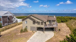 A beachfront house with a balcony overlooking the ocean, a driveway leading to the entrance, and a neighboring building. - Pelican's Way - 4 BR Oceanfront Cottage in Southern Shores (Southern Shores)