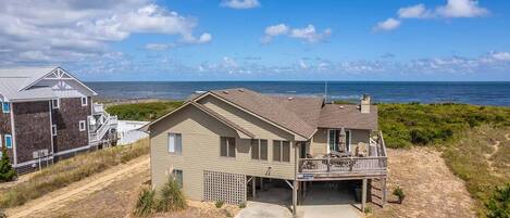 A beachfront house with a balcony overlooking the ocean, a driveway leading to the entrance, and a neighboring building.